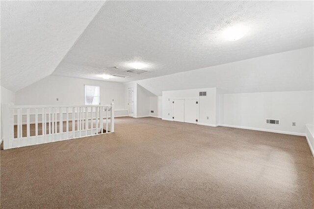 additional living space with vaulted ceiling, carpet flooring, and a textured ceiling