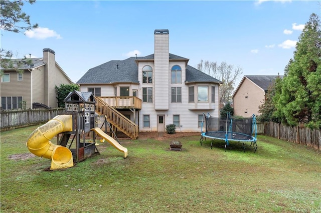 rear view of property with a trampoline, a playground, and a lawn