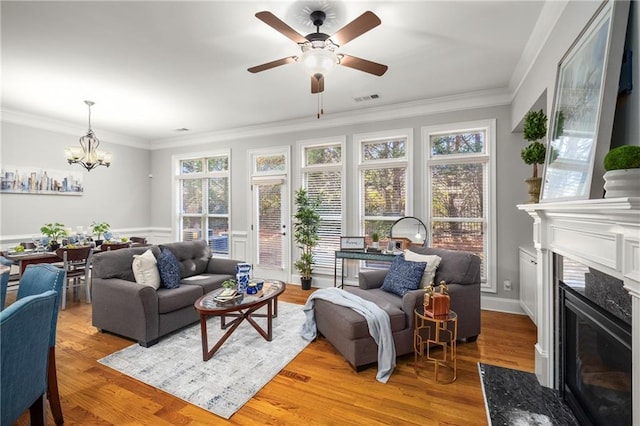 living room featuring ceiling fan with notable chandelier, a premium fireplace, visible vents, light wood-style floors, and crown molding