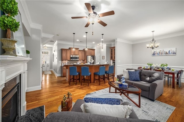 living room with baseboards, a premium fireplace, crown molding, light wood-type flooring, and ceiling fan with notable chandelier