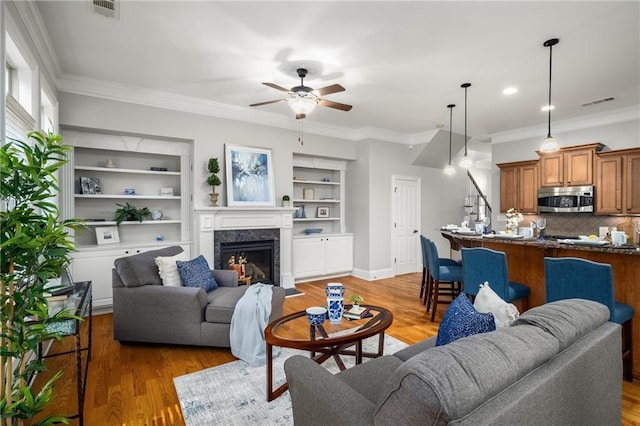 living area featuring visible vents, ceiling fan, crown molding, light wood-type flooring, and a fireplace