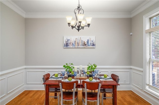 dining room featuring a wainscoted wall, crown molding, light wood-style flooring, and an inviting chandelier