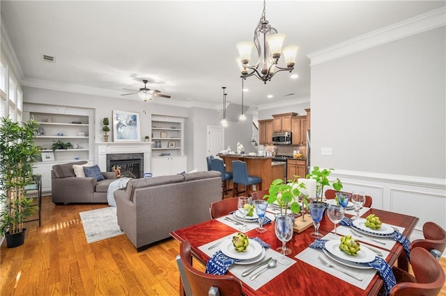 dining room featuring visible vents, ornamental molding, built in shelves, and light wood-style floors