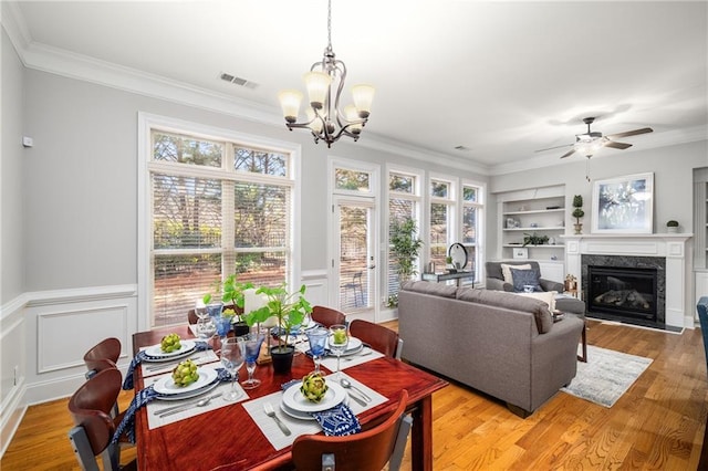 dining area featuring built in shelves, a high end fireplace, visible vents, ornamental molding, and light wood-type flooring