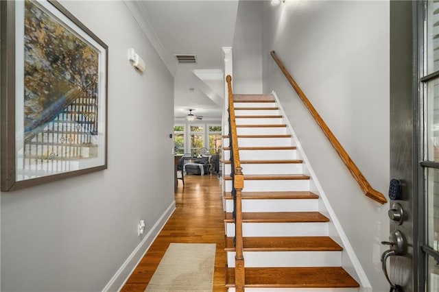 staircase featuring ornamental molding, visible vents, baseboards, and wood finished floors