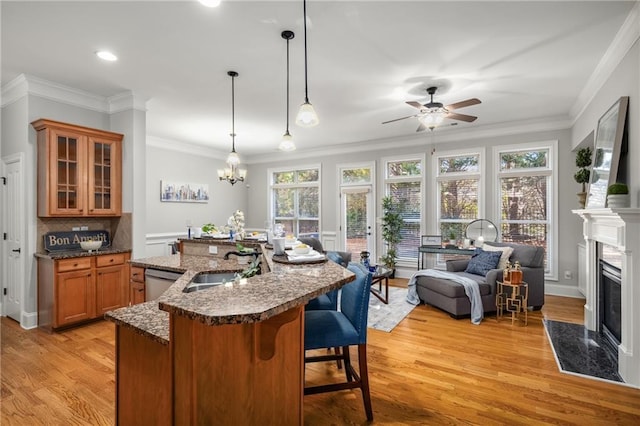 kitchen with a breakfast bar, a sink, a high end fireplace, stainless steel dishwasher, and brown cabinetry