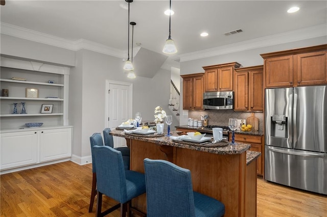 kitchen featuring visible vents, appliances with stainless steel finishes, brown cabinetry, light wood-style floors, and dark stone countertops