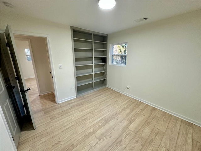 unfurnished bedroom featuring baseboards, light wood-style flooring, visible vents, and a closet