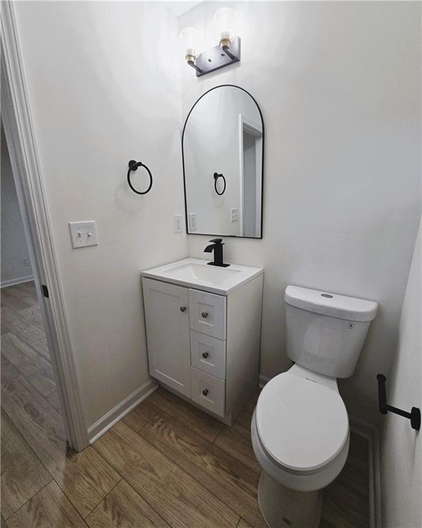 bathroom with baseboards, vanity, toilet, and wood finished floors