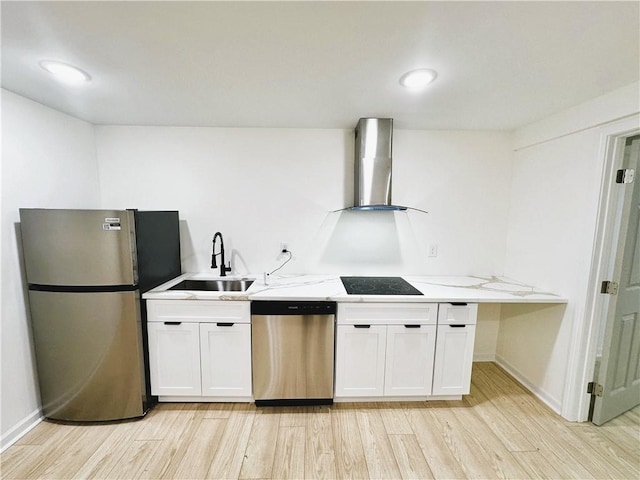 kitchen with wall chimney range hood, a sink, appliances with stainless steel finishes, and white cabinets