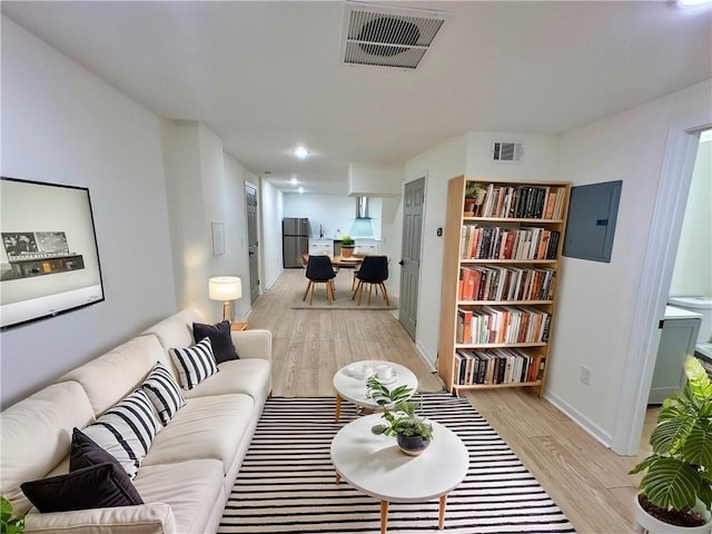 living room featuring light wood-type flooring, electric panel, visible vents, and baseboards