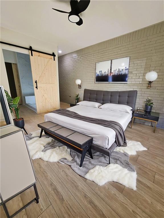 bedroom with wood finished floors, brick wall, and a barn door