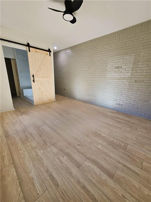 unfurnished room featuring brick wall, a barn door, and wood finished floors