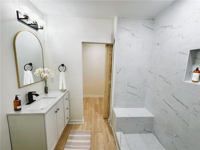 bathroom with tiled shower, wood finished floors, and vanity