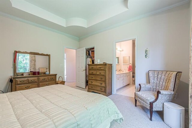 bedroom featuring connected bathroom, a raised ceiling, light carpet, and a spacious closet