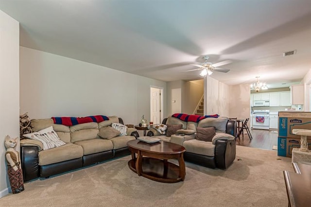 carpeted living room with ceiling fan with notable chandelier