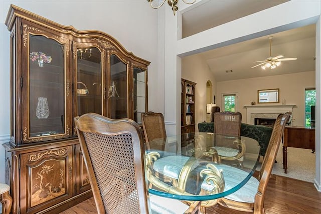 dining room featuring ceiling fan, a high end fireplace, dark hardwood / wood-style flooring, and vaulted ceiling