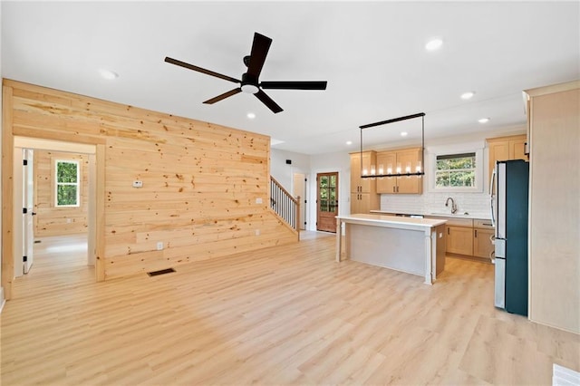 kitchen with decorative light fixtures, light wood-type flooring, stainless steel refrigerator, a kitchen island, and sink