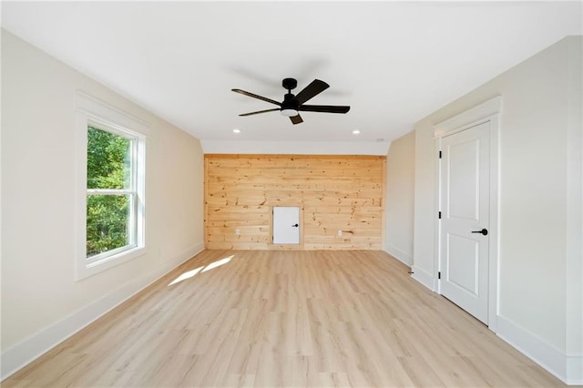 unfurnished living room featuring light wood-type flooring, ceiling fan, and wooden walls