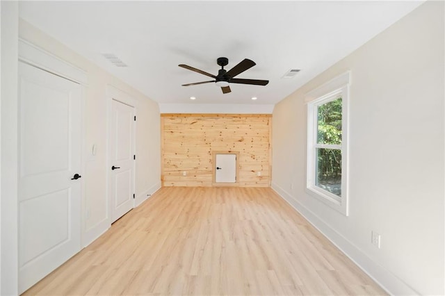 unfurnished living room with ceiling fan, light hardwood / wood-style floors, and wooden walls