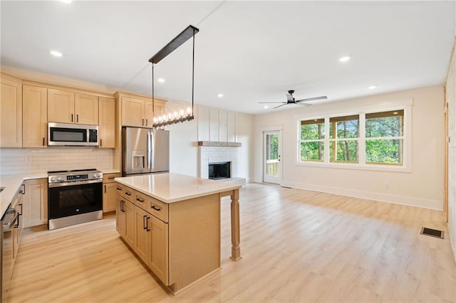 kitchen featuring decorative light fixtures, ceiling fan, a center island, light wood-type flooring, and appliances with stainless steel finishes