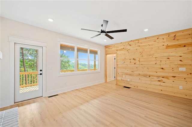 unfurnished room featuring ceiling fan, wood walls, and light hardwood / wood-style floors