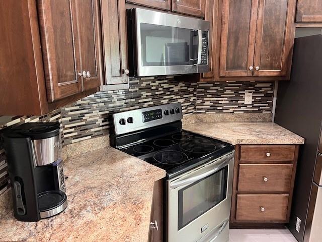 kitchen with dark brown cabinets, light stone countertops, stainless steel appliances, and tasteful backsplash