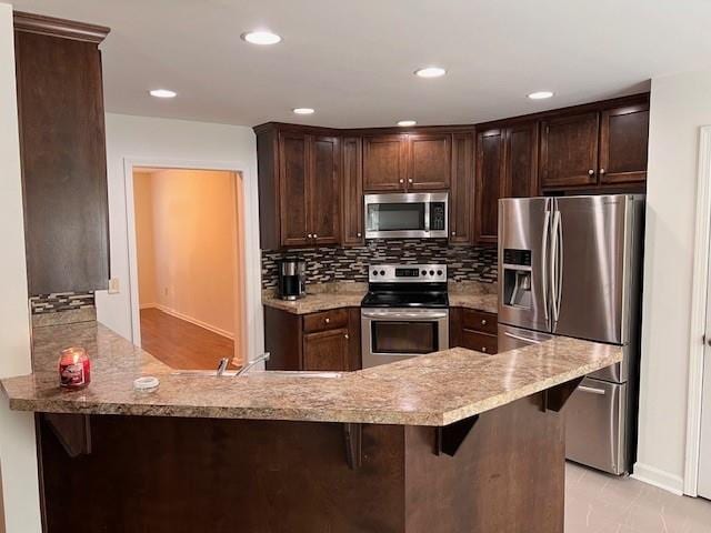 kitchen with dark brown cabinets, tasteful backsplash, kitchen peninsula, a kitchen breakfast bar, and stainless steel appliances