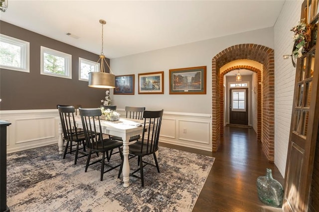 dining space featuring a healthy amount of sunlight, brick wall, and dark hardwood / wood-style floors