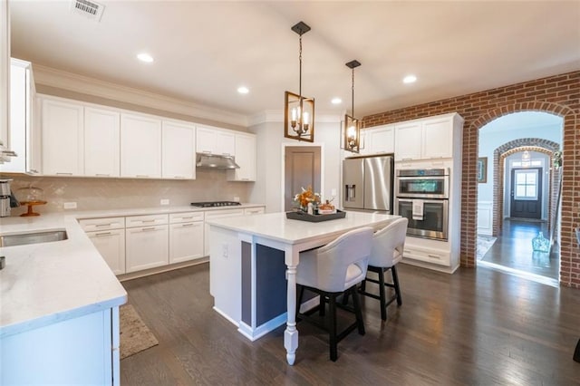 kitchen with brick wall, stainless steel appliances, a kitchen island, and white cabinets