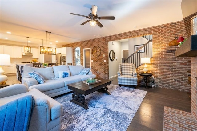 living room featuring brick wall, dark wood-type flooring, and ceiling fan with notable chandelier