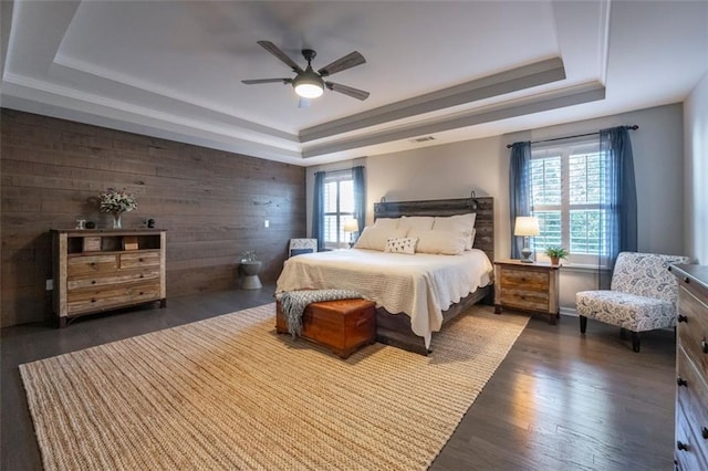 bedroom featuring ceiling fan, a raised ceiling, multiple windows, and wood walls