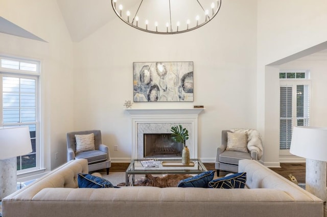 living room with high vaulted ceiling, a notable chandelier, wood-type flooring, and a premium fireplace