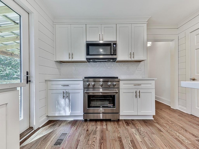 kitchen with white cabinets, wooden walls, stainless steel appliances, and light hardwood / wood-style floors