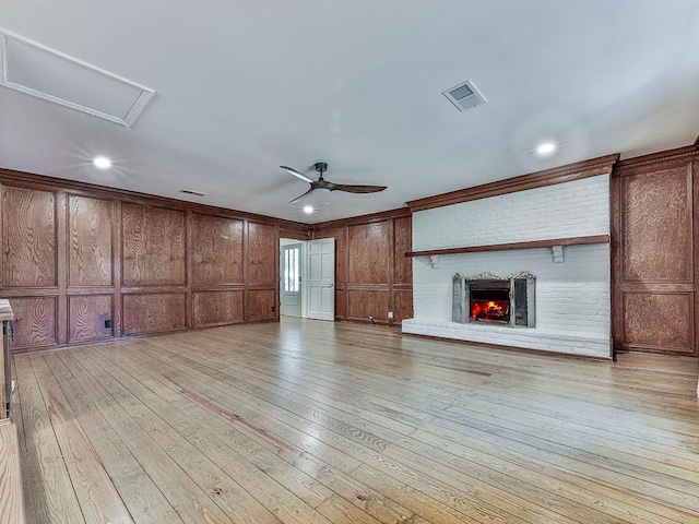 unfurnished living room with a brick fireplace, light hardwood / wood-style flooring, ceiling fan, and wooden walls