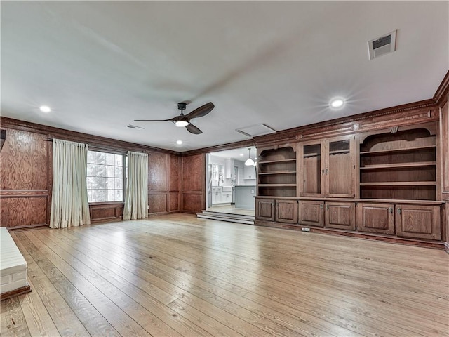 unfurnished living room with ceiling fan, built in features, crown molding, and light wood-type flooring