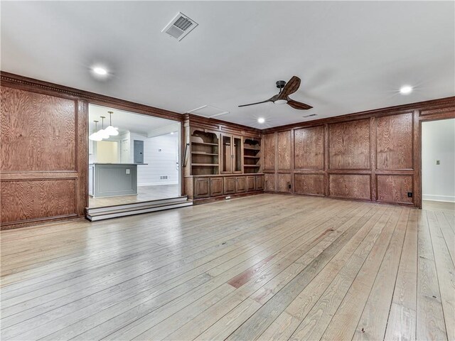 unfurnished living room featuring ceiling fan, built in features, electric panel, wooden walls, and light wood-type flooring