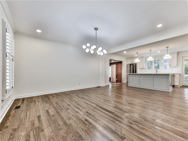 unfurnished living room with wood-type flooring, an inviting chandelier, ornamental molding, and sink