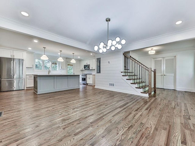 unfurnished living room featuring an inviting chandelier, sink, crown molding, wooden walls, and light hardwood / wood-style floors