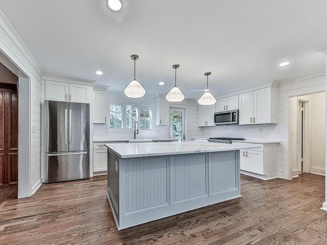 kitchen with dark wood-type flooring, white cabinets, crown molding, hanging light fixtures, and stainless steel appliances