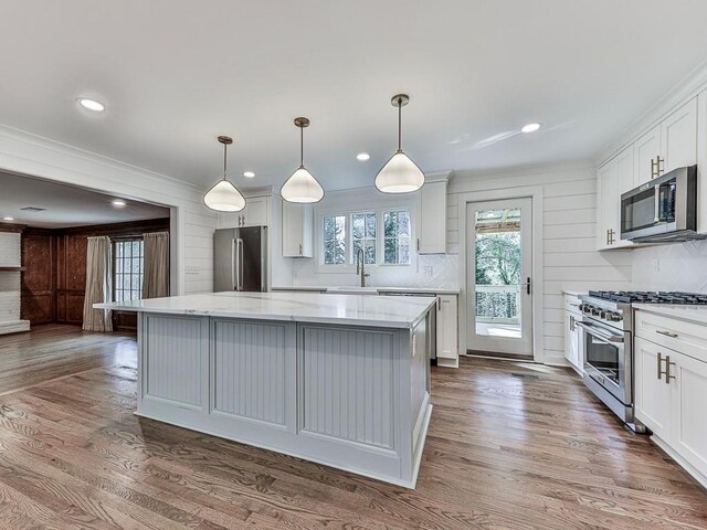 kitchen with a center island, hardwood / wood-style floors, decorative light fixtures, high quality appliances, and white cabinets