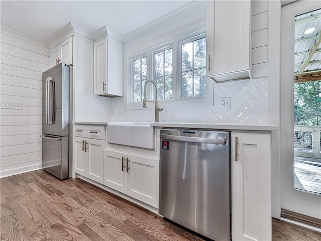 kitchen with stainless steel appliances, wooden walls, sink, light hardwood / wood-style flooring, and white cabinetry