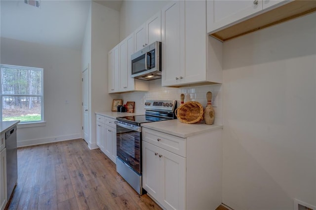 kitchen featuring light wood finished floors, tasteful backsplash, appliances with stainless steel finishes, light countertops, and white cabinetry