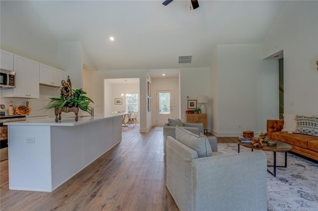 living area with visible vents, stairway, light wood-style floors, vaulted ceiling, and ceiling fan with notable chandelier