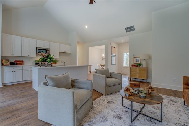 living area featuring high vaulted ceiling, light wood-style flooring, and visible vents