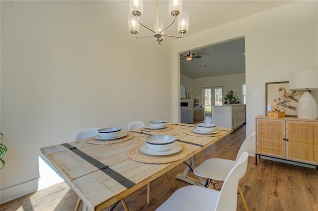 dining space with wood finished floors and ceiling fan with notable chandelier