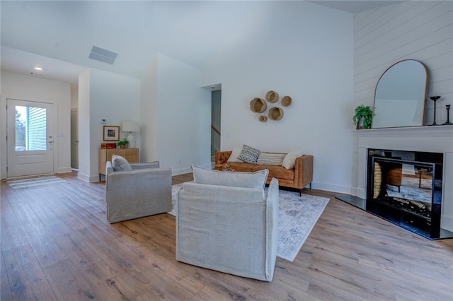 living room with a high ceiling, wood finished floors, baseboards, stairs, and a glass covered fireplace