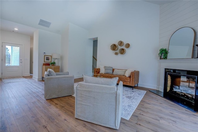 living room featuring visible vents, a towering ceiling, a glass covered fireplace, wood finished floors, and baseboards