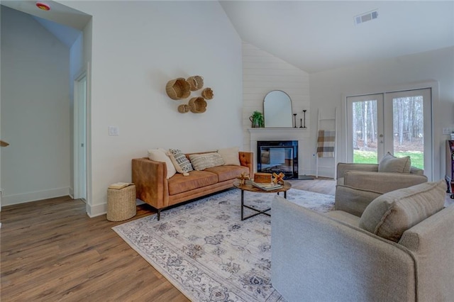 living room featuring baseboards, visible vents, a glass covered fireplace, wood finished floors, and high vaulted ceiling