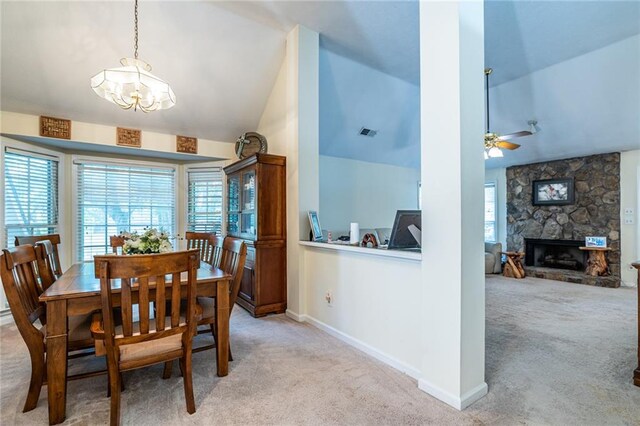 carpeted dining space with a stone fireplace, ceiling fan with notable chandelier, and lofted ceiling